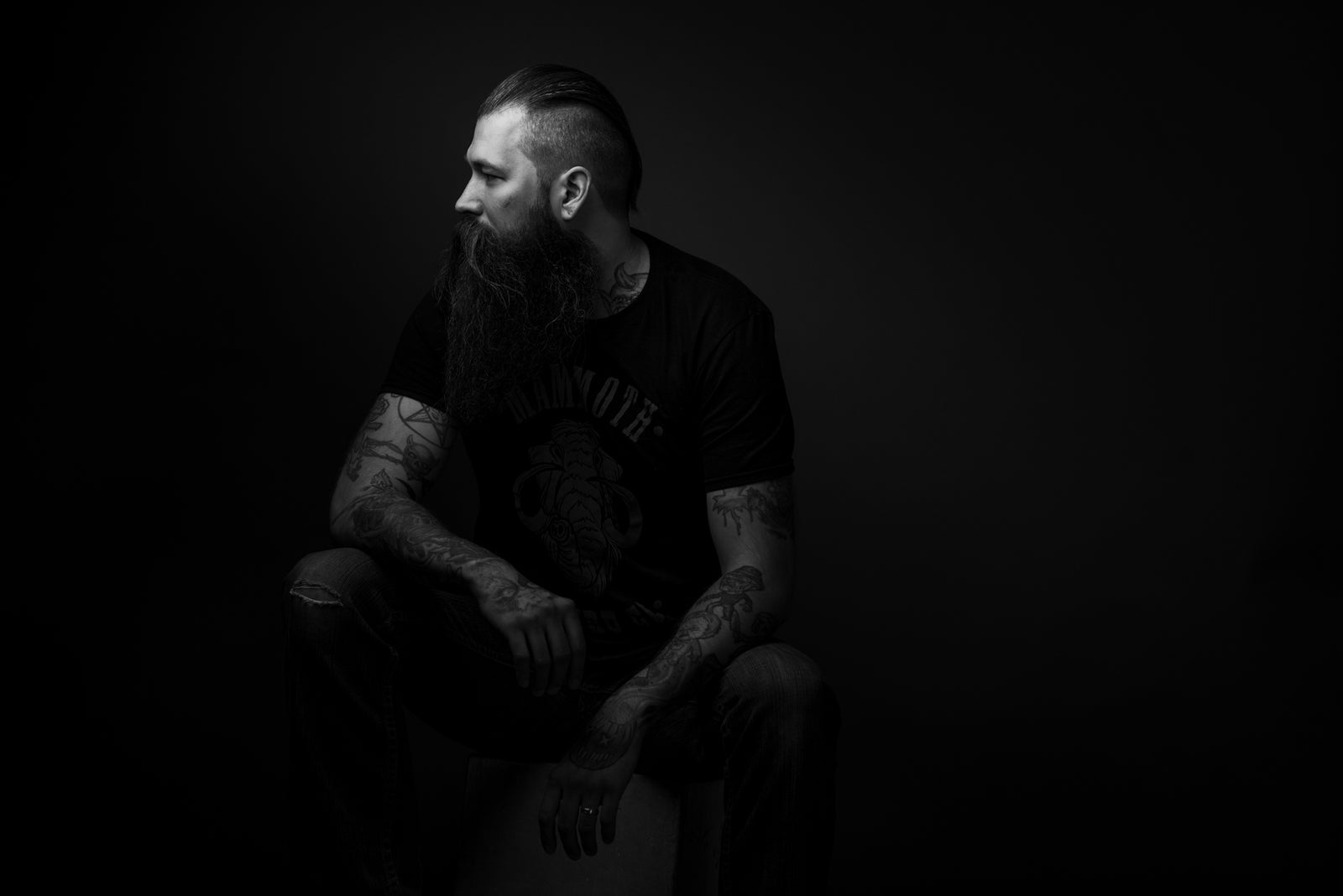 Bearded man wearing Mammoth Beard Co. t-shirt, showcasing premium beard care products, sitting against a dark background